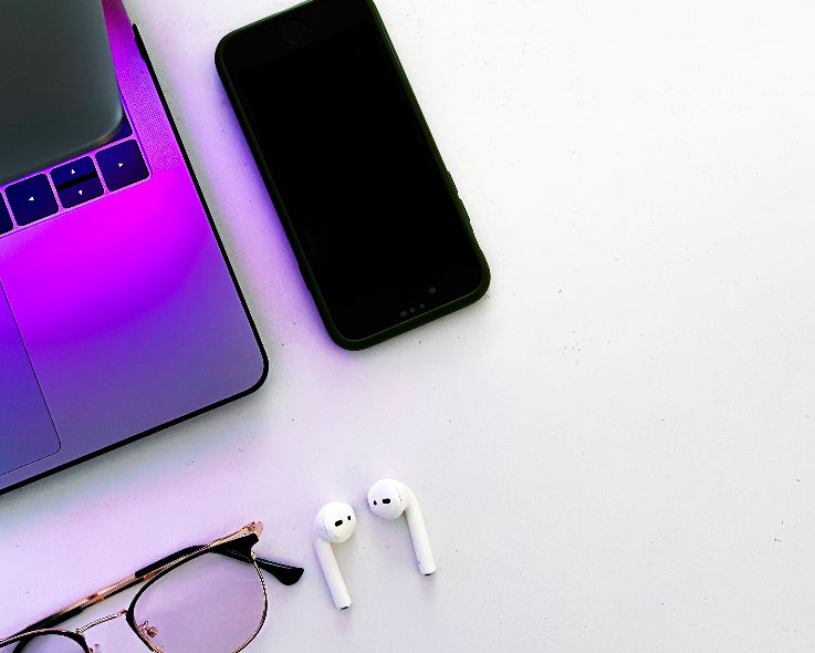 Laptop, smartphone, sunglasses, and wireless earbuds on a white surface